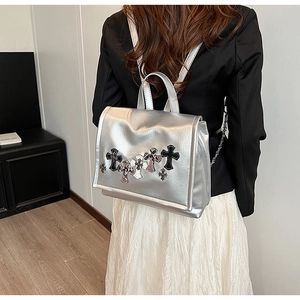 Dettaglio dello zaino in pelle argento con diverse toppe a croce in stile punk sulla patta