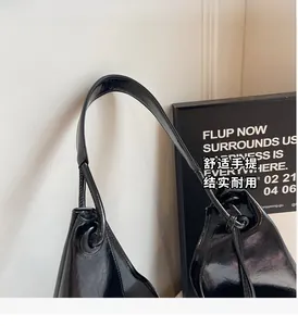 Detail of the high-gloss black leather handle and metal ring attachment on the tote bag