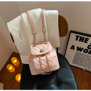 Détail d'un mini sac à dos matelassé rose avec breloques dorées sur une chaise en bois