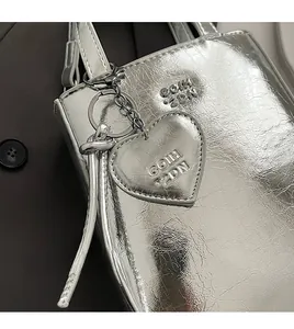 Détail d'un sac seau argenté métallisé en cuir plissé avec breloque en cœur