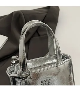 Détail du sac à main argenté texturé avec fermeture éclair et logo COIN ADON embossé
