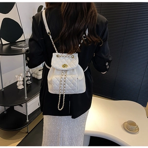Detail of white quilted backpack with gold chain straps and turn-lock closure on front pocket