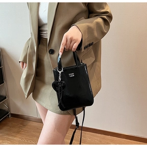 Détail du petit sac carré noir brillant avec breloque cœur et bandoulière réglable fine