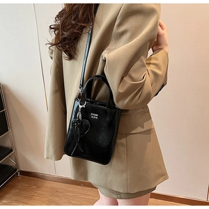 Détail du sac à bandoulière en cuir verni noir avec charm cœur et logo blanc gravé
