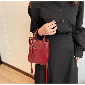 Détail du petit sac carré en cuir verni rouge avec breloque cœur porté par le mannequin