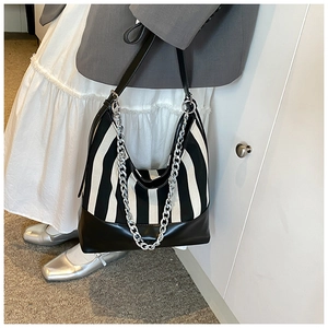 Detail of striped tote bag with silver chain accessory and leather straps in a chic outfit