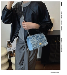 Détail de la texture denim matelassée et de la chaîne dorée du sac à rabat