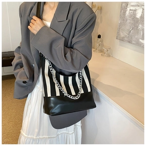 Detail of black and white striped tote bag featuring a bold silver chain and leather base