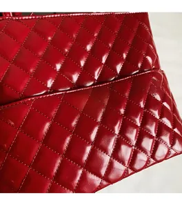 Detail of red quilted tote bag featuring glossy patent leather and a golden metal plaque