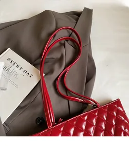 Detail of red quilted leather tote bag with slender straps on a brown blazer