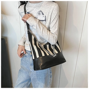 Detail view of striped canvas crossbody bag with silver chain strap on model