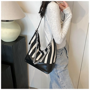 Detail of a black and white striped hobo bag with silver chain and leather bottom on model