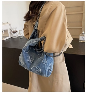 Detail of denim shoulder bag featuring white rose embroidery and dark metal chain strap