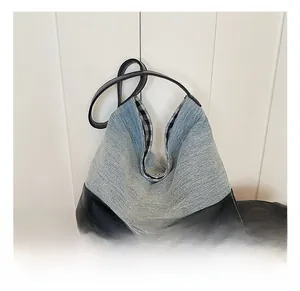 Detail of denim tote bag showing blue wash fabric, black leather straps and checkered lining