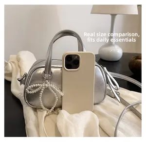 Silver metallic crossbody bag size comparison with smartphone and pearl bow detail
