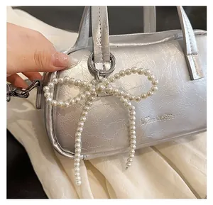 Close-up of a silver metallic handbag with a decorative woven pearl bow charm