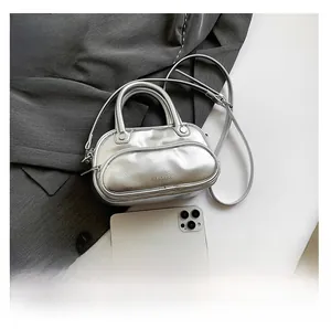 Silver metallic Boston bag with dual handles and logo detail on grey suit background