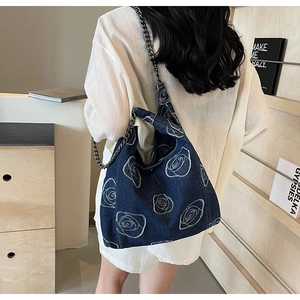 Denim shoulder bag with white rose embroidery and dark nickel chain strap on model