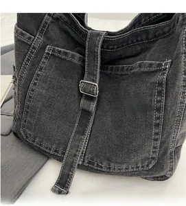 Detailed close-up of dark grey denim crossbody bag with contrast stitching and metal buckles