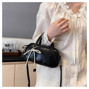 Close-up of black patent leather mini bag with a woven white pearl bow detail