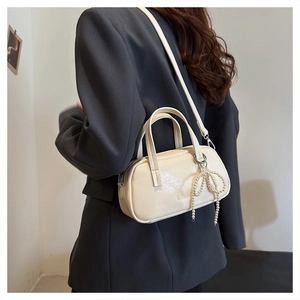 Close-up of beige Boston bag with pearl bow charm on gray blazer outfit