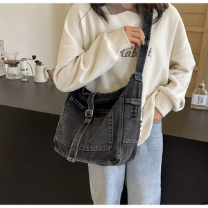 Detail of vintage washed black denim crossbody bag with flap buckle and distressed edges