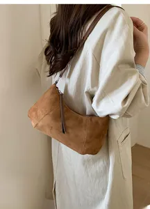 Détail d'un sac hobo en daim marron porté avec une fine bandoulière en cuir souple