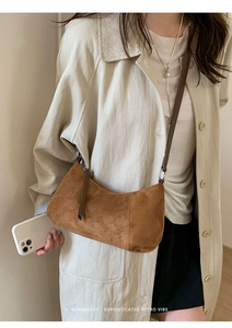 Détail d'un sac demi-lune en daim marron avec coutures verticales et bandoulière en cuir