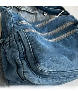 Detailed close-up of blue denim crossbody bag featuring multiple metal zippers and texture