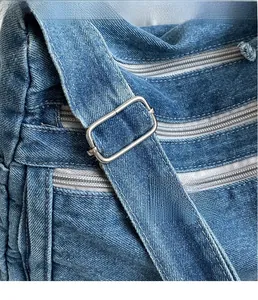 Detailed macro view of adjustable silver metal buckle and zipper on blue denim tote bag