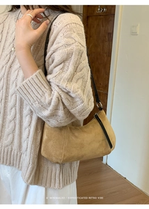 Gros plan d'un sac hobo en daim marron porté avec un pull en maille beige style rétro