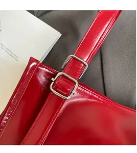 Close-up of red glossy leather tote bag showing adjustable strap and silver metal buckle