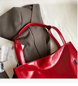 Detailed view of red glossy leather tote bag showing smooth texture and side zipper