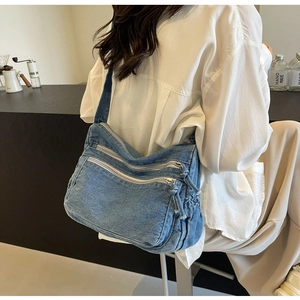 Detail of blue denim crossbody bag with multi-zipper pockets and drawstring detail