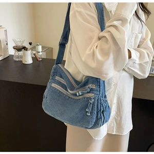 Detailed side view of washed blue denim crossbody bag with multiple zip pockets and drawstring