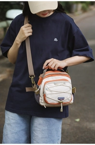 Close-up of orange and beige crossbody bag with adjustable drawstrings and woven strap