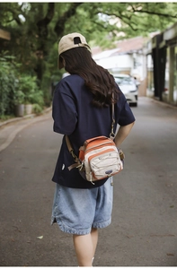 Outdoor street view of a multi-pocket orange hiking crossbody bag with bungee cord detail