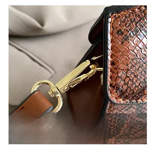 Close-up of golden rotating metal buckle and snake-textured strap on brown tote bag