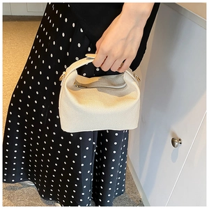 Detail of a creamy white textured canvas handbag with durable handles and gold-tone rings