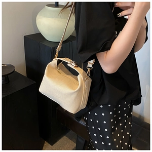 Detail showing beige woven crossbody bag with metallic gold clasp and texture