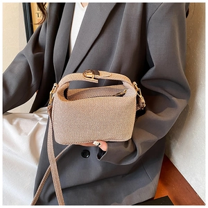 Detail of light brown woven texture handbag with gold metal clasp held by woman