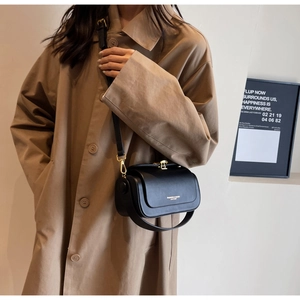 Detail of black leather crossbody bag with gold buckle on khaki trench coat