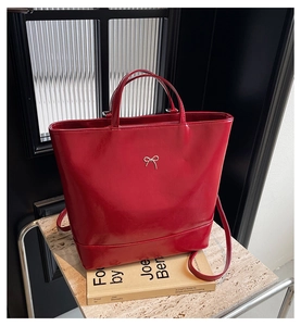 Detail of red glossy tote bag featuring a silver metal bow and leather texture