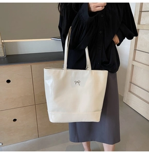 Detail of a large cream PU leather tote bag featuring a silver metal bow and shoulder strap