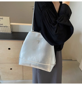 Detail view of a silver metallic tote bag with a bow accent and long shoulder strap