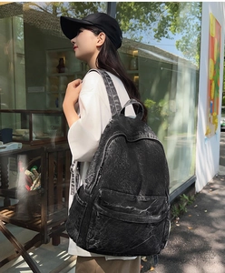 Detailansicht eines lässigen schwarzen Denim-Rucksacks, getragen von einem Modell im Freien