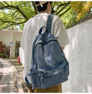 Detail view of a large navy denim backpack worn by a model in a natural outdoor setting