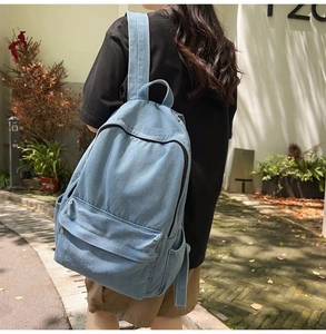 Outdoor lifestyle shot of a light blue denim backpack with large capacity and side pockets