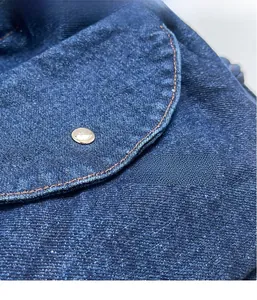 Nahaufnahme der dunkelblauen Denim-Struktur mit orangen Nähten und silbernem Metallknopf