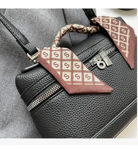 Close-up of black lychee grain leather bag with decorative silk scarf and silver padlock